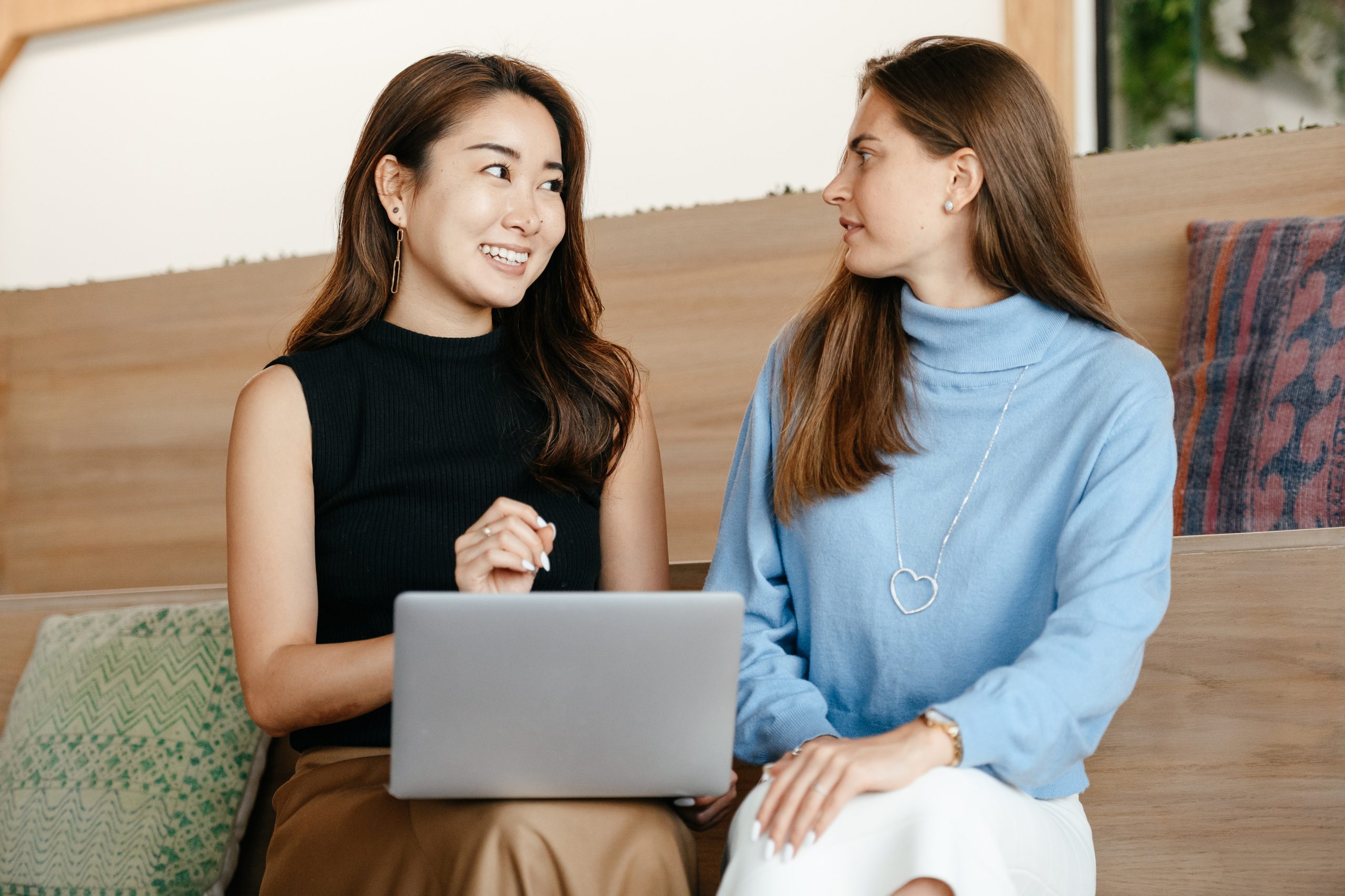 Two people sitting together. One is holding a laptop on their lap and the other one is facing her.