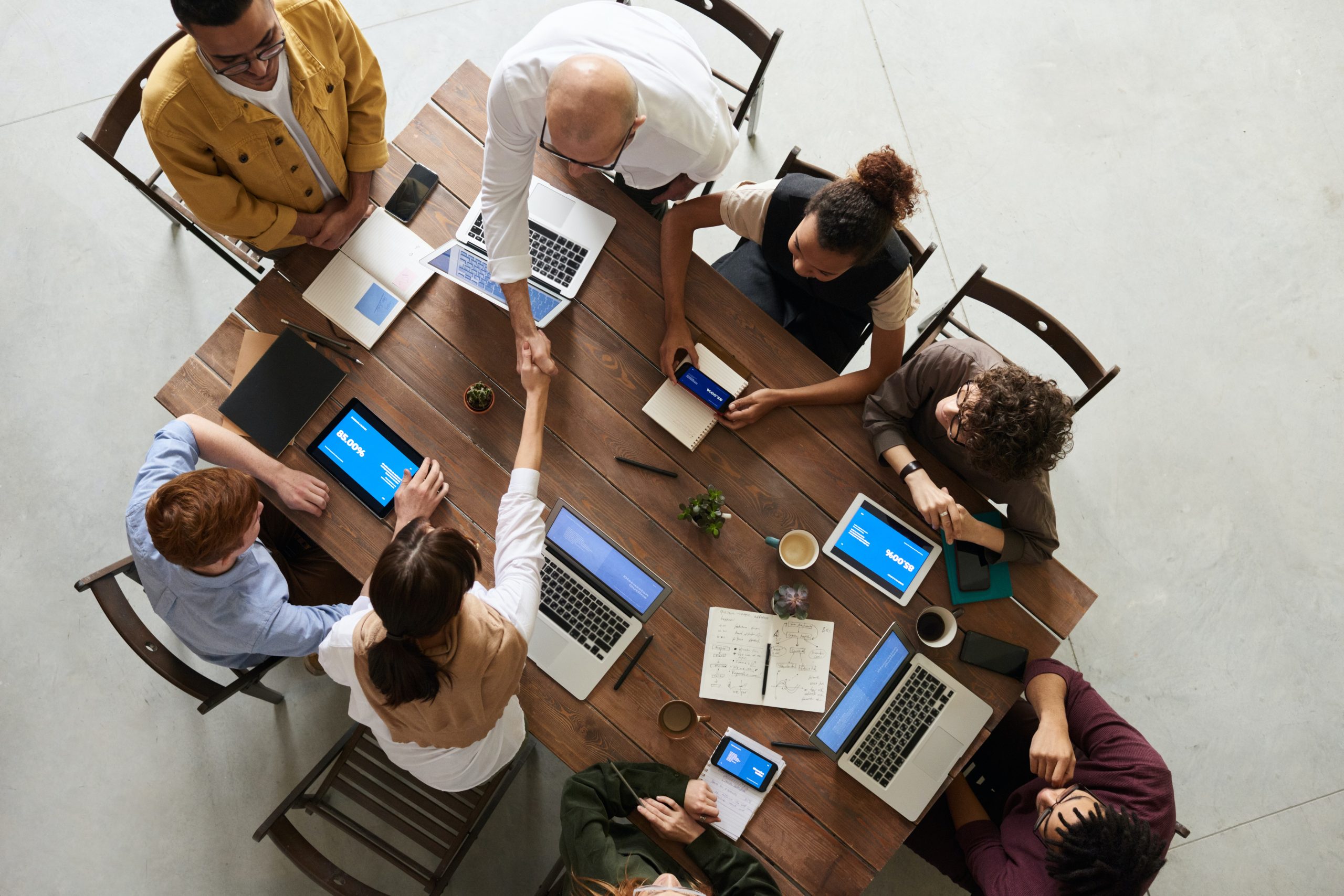 A top view picture of a group of people around a conference table. 2 of them are shaking hands.